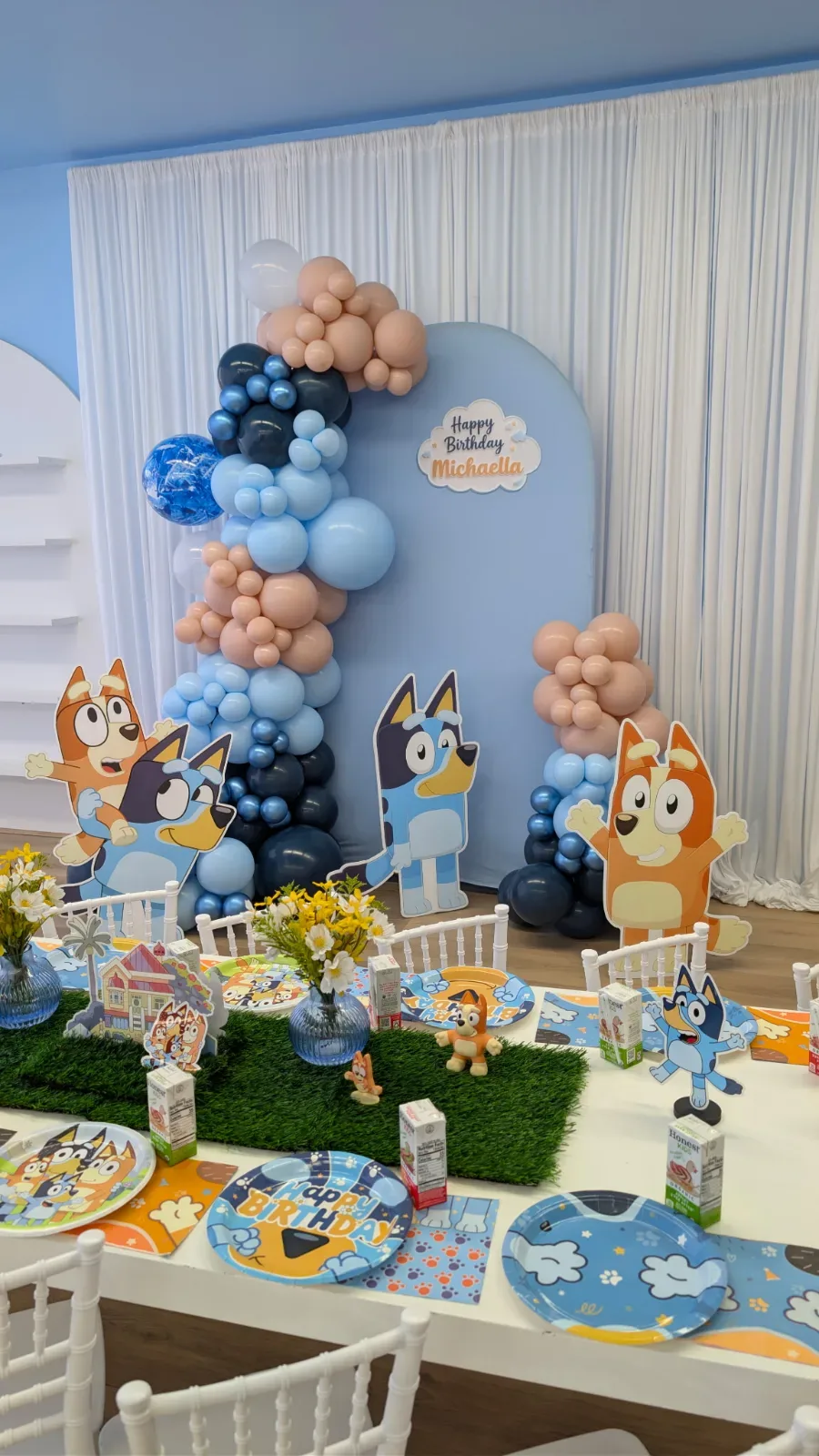 Mesa decorada con la temática de Bluey, que incluye un fondo con una guirnalda de globos y personajes de Bluey impresos.